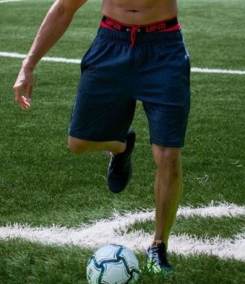 A man kicks a soccer ball while wearing red UFM underwear to reduce friction and prevent chafing.